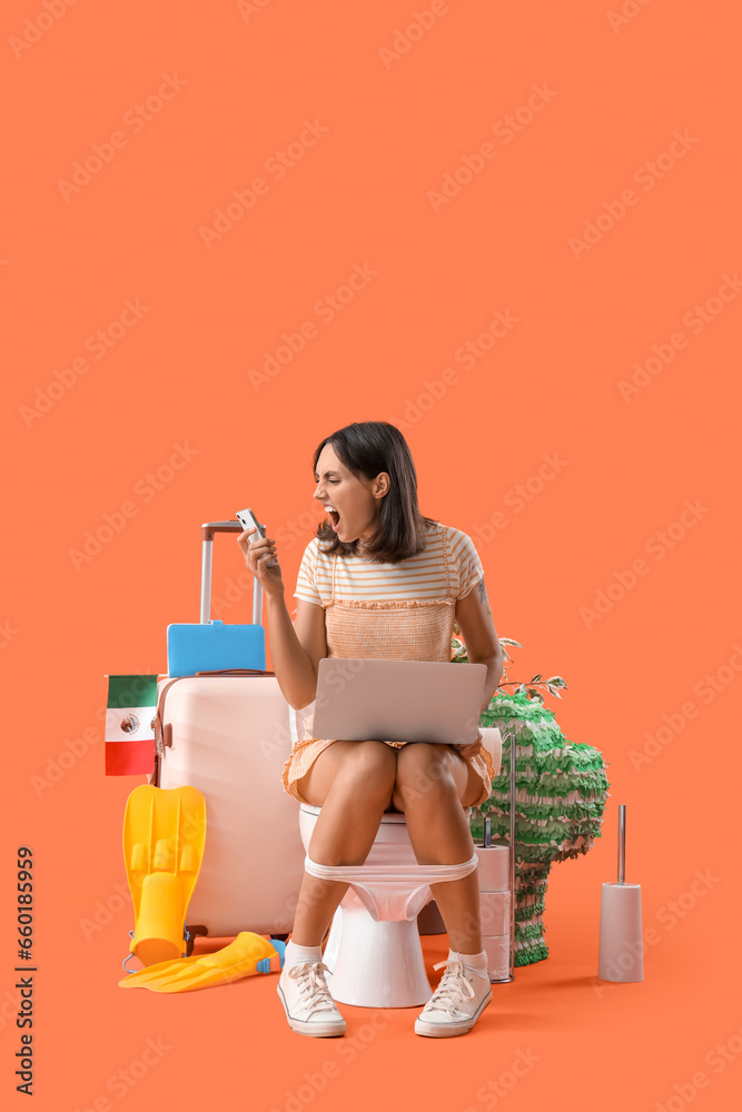 Angry young woman with mobile phone and laptop sitting on toilet bowl against orange background Angry young woman with mobile phone and laptop sitting on toilet bowl against orange background