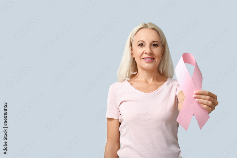 Mature woman with pink ribbon on grey background. Breast cancer awareness concept