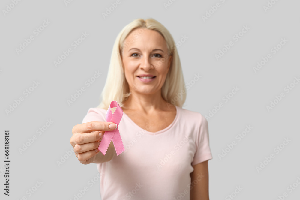 Mature woman with pink ribbon on grey background. Breast cancer awareness concept Mature woman with pink ribbon on grey background. Breast cancer awareness concept