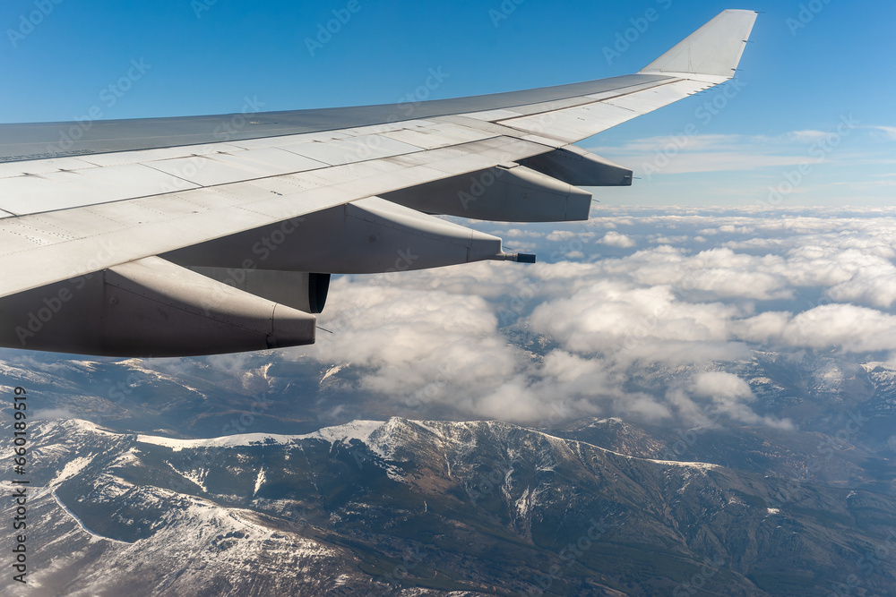 Blick auf die schneebedeckten Alpen mit feinen Wolken darüber aus einem Flugzeug