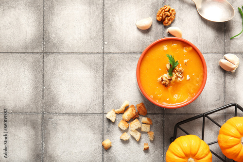 Bowl of delicious pumpkin cream soup with walnut, parsley and croutons on grey tile background