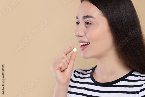 Happy woman taking pill on beige background, space for text