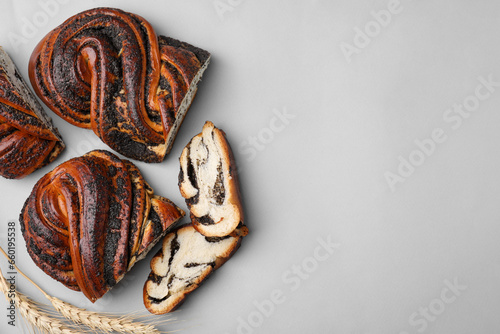 Pieces of poppy seed roll and spikelets on light grey background, flat lay with space for text. Tasty cake