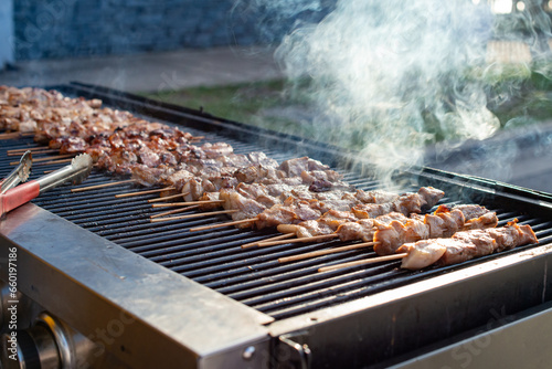 Multiple pieces of chicken skewers and pork kebabs grilling on a barbecue grill. There's smoke coming off the protein as it cooks. The appetizer food is in chunks on wooden sticks with barbeque sauce.
