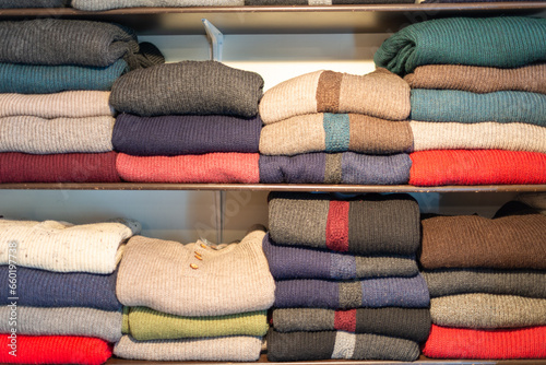 Multiple shelves of colorful natural wool, mohair, and cashmere knitted sweaters are on display.  The folded and stacked casual apparel are both cardigan and pullover styles for sale in a retail shop. photo