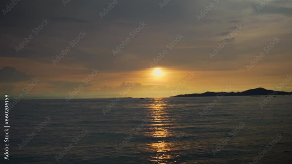 Pattaya Beach Sunset In Thailand; Ascending Shot Over The Coastal Horizon With A Golden Sunlight Reflecting Off The Water and a person riding a jet ski Pattaya Beach Sunset In Thailand; Ascending Shot Over The Coastal Horizon With A Golden Sunlight Reflecting Off The Water and a person riding a jet ski