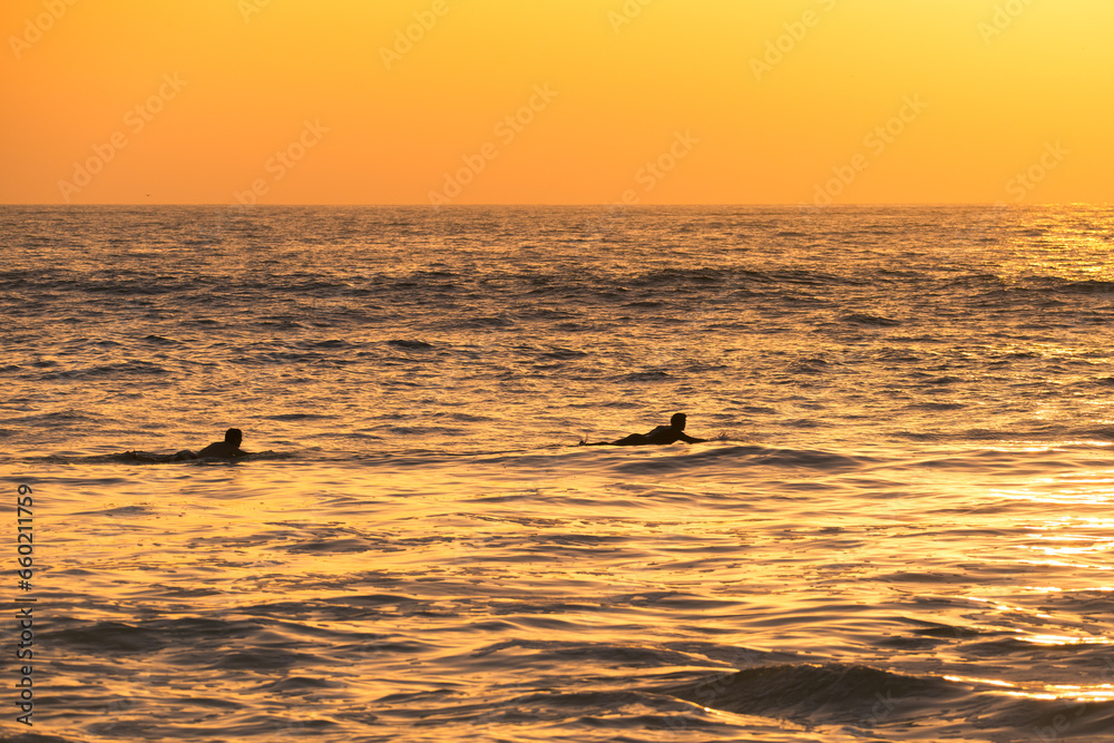 Surfer silhouettes in the ocean at sunset