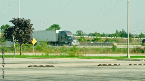 Slow motion of a grey semi truck trailer driving on interstate. Hiring Truck drivers concept. American trucking business. Trees in foreground photo