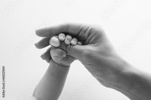 Parents' hands hold the fingers of a newborn baby. The hand of a mother and father close-up holds the fist of a newborn baby. Family health and medical care. Tiny fingers in a black and white photo.
