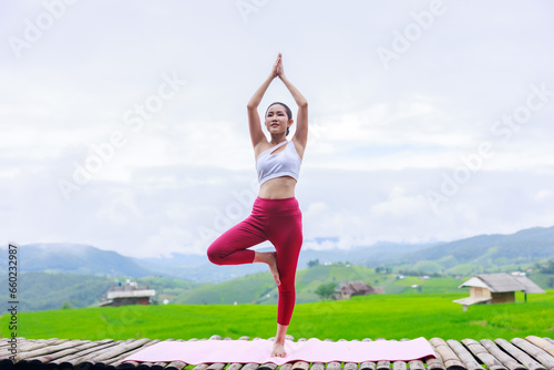 young girl is doing yoga on balcony of resort with rice terraces, Ban Pa Bong Piang and mountains green over white sky in rainy season, Travel healthy lifestyle, enjoying in nature concept,