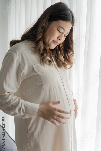 Pregnant asian woman holds hands on belly touching her baby caring about her health Beautiful happy pregnant woman tender mood photo of pregnancy