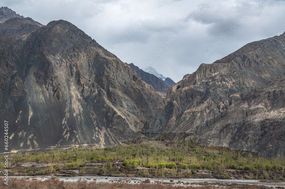 Scenic view of Himalayas and Ladakh ranges. Beautiful barren hills in Ladakh with dramatic clouds in the background. Road side view, Shyok river , rocks and greenery in base of the mountains. Scenic view of Himalayas and Ladakh ranges. Beautiful barren hills in Ladakh with dramatic clouds in the background. Road side view, Shyok river , rocks and greenery in base of the mountains.