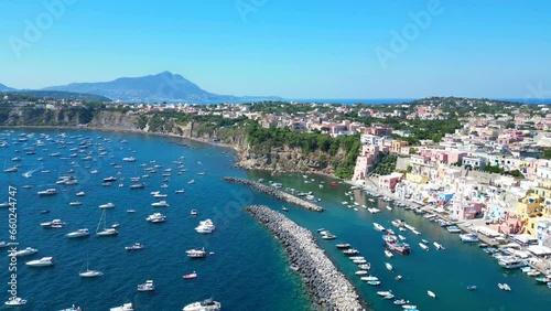 Impressive aerial pullback from Panoramica sulla Corricella on Procida Island (Isola di Procida) of the blue Tyrrhenian Sea in the Gulf of Naples with pastel buildings, white boats and mighty Vesuvius photo