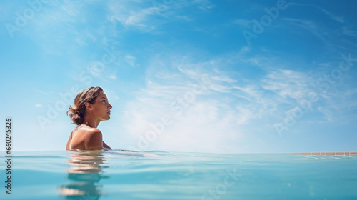 Back view of young woman in bikini on the sun-tanned slim, shapely body with her arms spread to the side, relaxing in swimming pool on the roof top of hotel, enjoy cityscape at sunset. photo