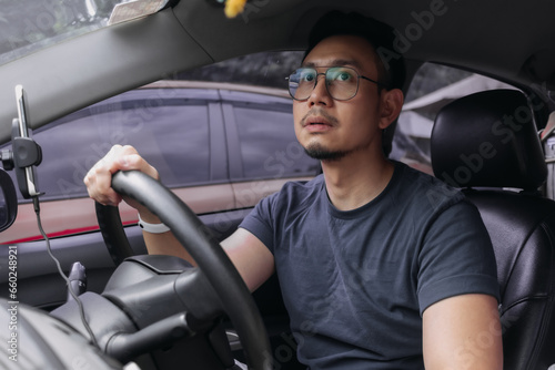 Asian Thai man with beard, wear eyeglasses parking a car, looking at rear view mirror while driving training.