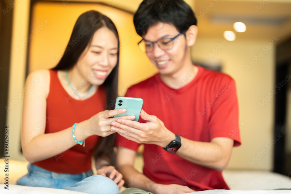 Hand shot of an Asian male and female online business owner. holding a smartphone together To gain knowledge and order products on the shopping platform wearing a red shirt In the hotel bedroom Hand shot of an Asian male and female online business owner. holding a smartphone together To gain knowledge and order products on the shopping platform wearing a red shirt In the hotel bedroom