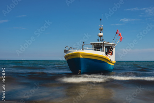 Fototapeta Naklejka Na Ścianę i Meble -  Fishing boat on the beach in Sopot, Poland. Magnificent long exposure calm Baltic Sea. Wallpaper defocused waves. Fishermans sea bay Vacation and holidays. travel attraction tourist destination 