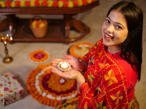 A young Indian woman holding an oil lamp at home - Diwali celebration  rangoli making  festivals. A beautiful female making rangoli and decorating it with a Diwali oil lamp at home - Diwali festiva...