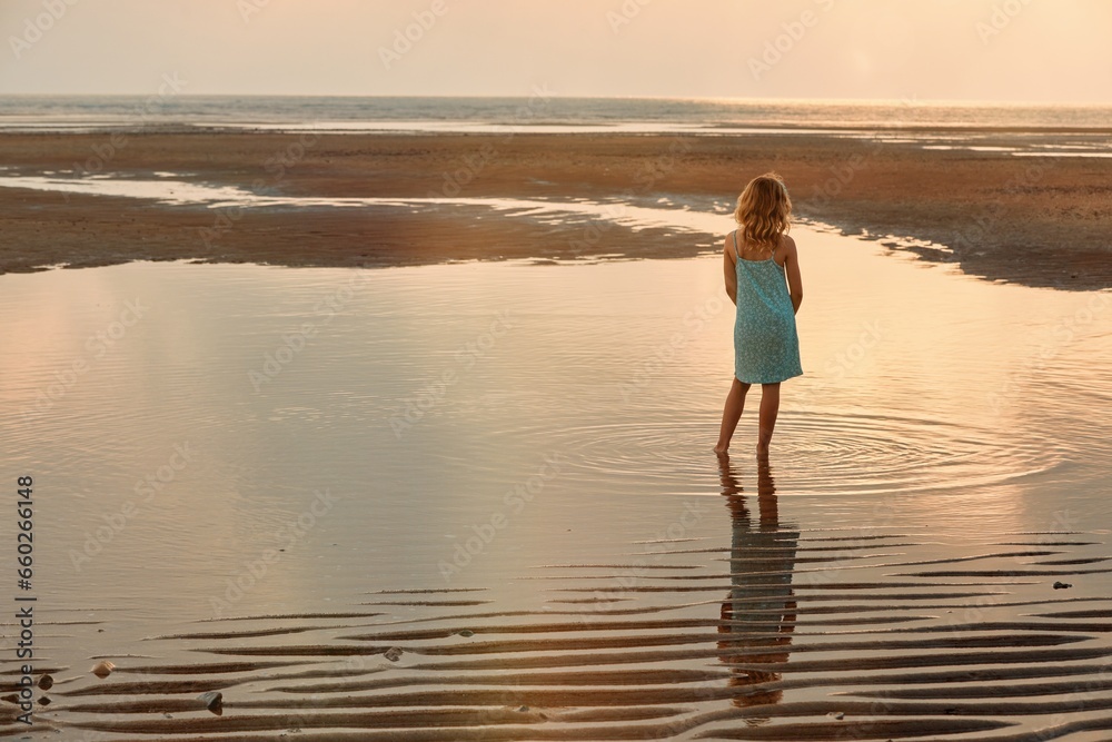 A young girl plays in a pool of water left by the ocean tide as it recedes 