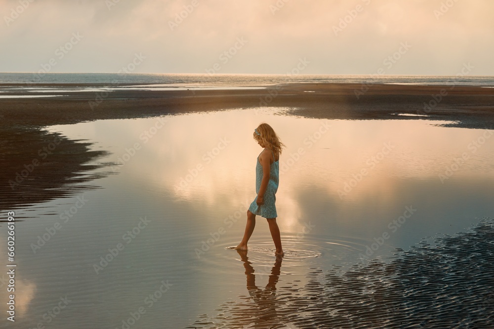 Fototapeta premium A young girl plays in a pool of water left by the ocean tide as it recedes 