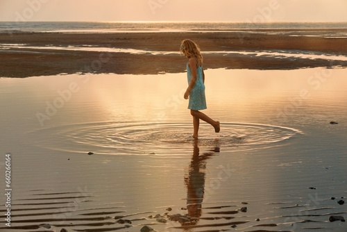 A young girl plays in a pool of water left by the ocean tide as it recedes 