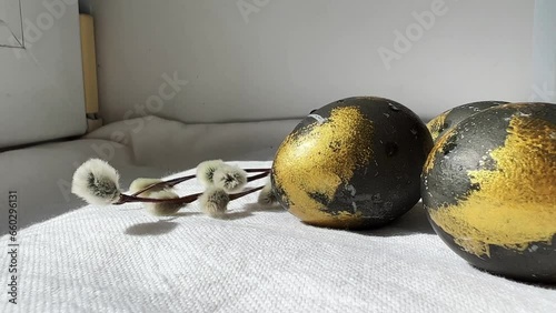 Cosmic eggs with gold are lying on a white tablecloth next to willow twigs for Easter