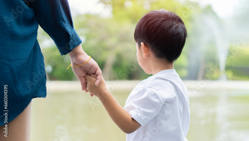 Cropped image of Asian mother holding hand of her little son outdoors.