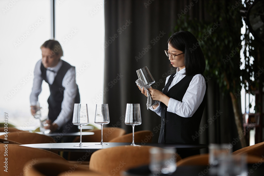Side view portrait of young Asian woman polishing wine glass in luxury restaurant setting, copy space Side view portrait of young Asian woman polishing wine glass in luxury restaurant setting, copy space