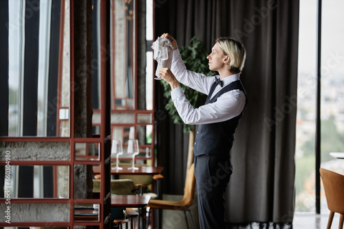 Side view portrait of elegant waiter polishing glasses in luxury restaurant interior, copy space © Seventyfour