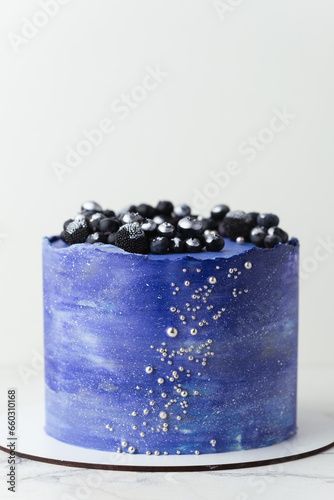 Birthday cake with blue cream cheese frosting decorated with blueberries covered with silver kandurin. Cosmic cake or space themed cake on the white background. photo