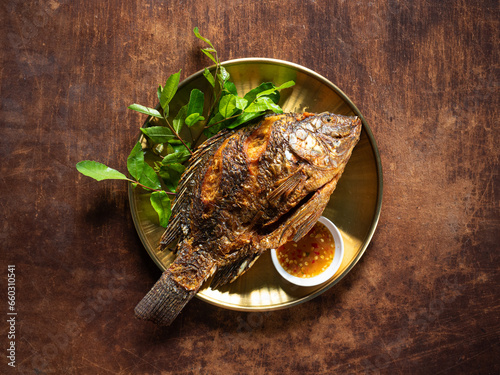 top view dish of deep fried whole Tilapia fish with dipping sauce and fresh vegetables
