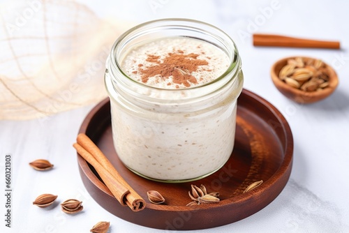 close-up of overnight oats in clear glass jar, cinnamon sticks beside