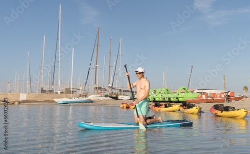 Young, sexy, Latin American man kneeling on a paddle board doing water sports.