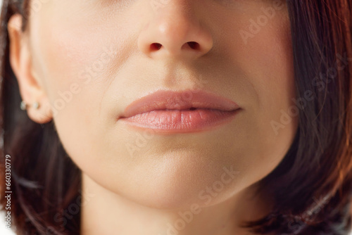 Close up cropped photo of young female face, lips without lipstick. Mouth is closed. Natural gloss of lips and woman's skin. Increase in lips, cosmetology.