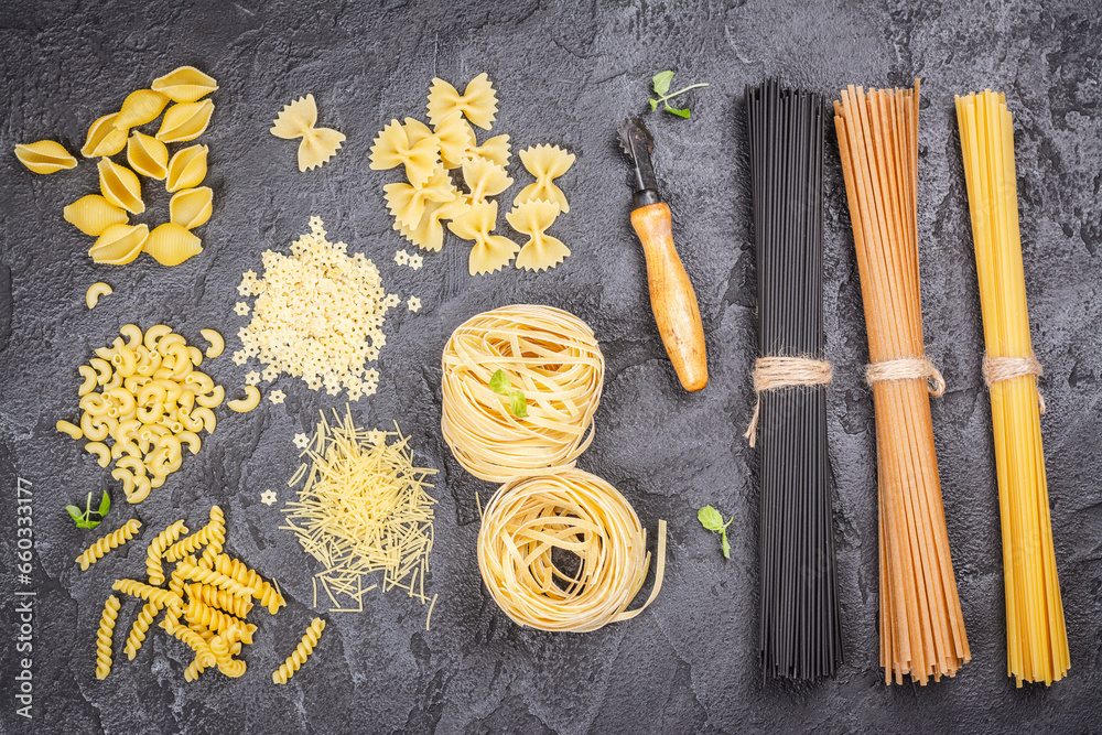 Pasta month. Assortment of uncooked pasta and noodles over black stone background, top view with
