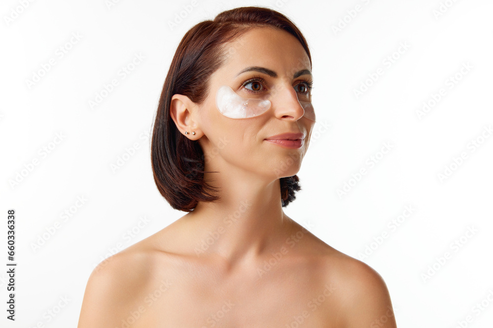 Portrait of young charming brunette woman with bare shoulders, eyes patches over white studio background. Concept of beauty, natural make-up, skin care Portrait of young charming brunette woman with bare shoulders, eyes patches over white studio background. Concept of beauty, natural make-up, skin care