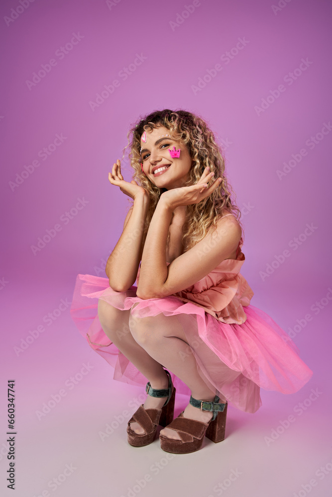 lovely jolly woman in pink costume of tooth fairy with face stickers squatting raising hands to face lovely jolly woman in pink costume of tooth fairy with face stickers squatting raising hands to face