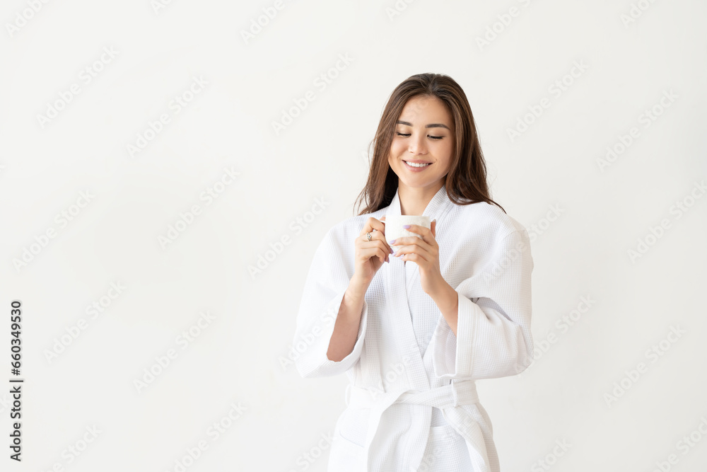 Beautiful Asian woman in white robe with coffee, relaxing after taking shower on white wall background. Beautiful Asian woman in white robe with coffee, relaxing after taking shower on white wall background.