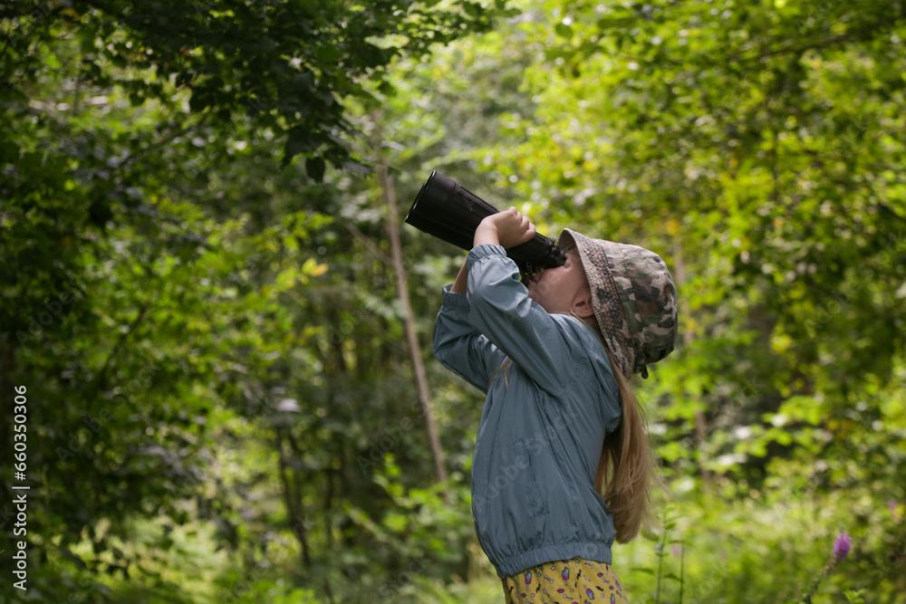 Cute little girl exploring nature looking through binoculars. Child playing outdoors. Kids travel, adventure and bird watching concept. Cute little girl exploring nature looking through binoculars. Child playing outdoors. Kids travel, adventure and bird watching concept.