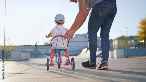 father teaches son baby to ride a children bike. happy family kid dream concept. baby baby rides a bike dad helps. father's day concept. child lifestyle playing riding a bike outdoors