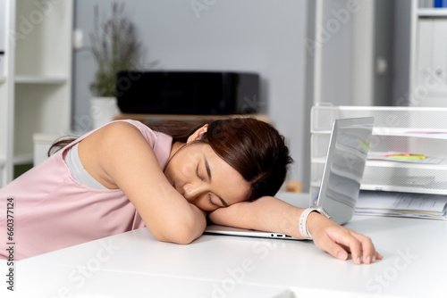 Young adult Asian businesswoman sleeping on her desk with a computer pc in the office setting background. - Workaholic, boring, exhausted, sleepy business woman concept