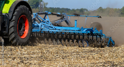 The tractor works in the field with a plow with a disc harrow. Seasonal tillage for subsequent sowing of grain. Photo series