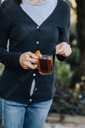 Preparing tea in a bag in a cup of water in a woman's hands outdoors. Food photography, portrait.