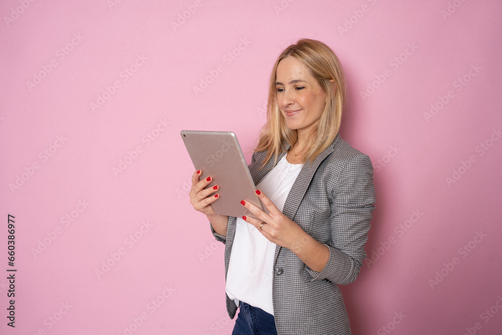 Portrait of happy young blonde business woman using tablet isolated against pink background. Smiling pretty girl holding a digital tablet computer. Modern technologies and business Portrait of happy young blonde business woman using tablet isolated against pink background. Smiling pretty girl holding a digital tablet computer. Modern technologies and business