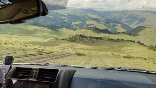 Dangerous descent down by car with a beautiful view. The SUV goes down a steep slope with green grass. Mountains and forest are visible in the distance. The river runs. The sky is in the clouds.