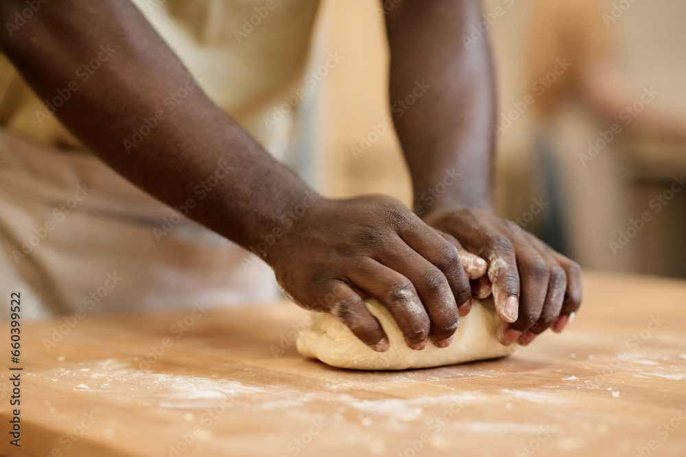 Close up of young Black man kneading dough while making fresh bread in artisan bakery, copy space