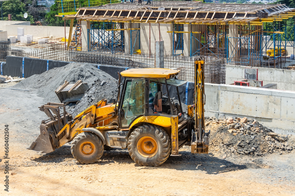 The excavator backfills the pit with the front bucket. Moves soil around the construction site. Foundation reinforcement first floor. Heavy construction equipment The excavator backfills the pit with the front bucket. Moves soil around the construction site. Foundation reinforcement first floor. Heavy construction equipment