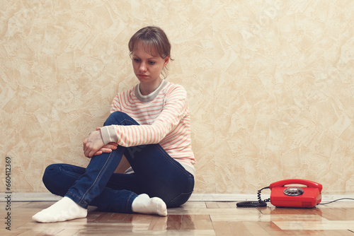 Fotografía Shot of unhappy young woman sitting near red telephone