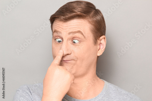 Portrait of funny man making goofy face, touching his nose with finger
