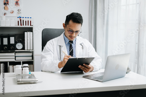 Wallpaper Mural Physician doctor sit on table in hospital. Attractive therapist male practitioner pharmacist smile and use tablet and laptop. after success work from treatment Torontodigital.ca
